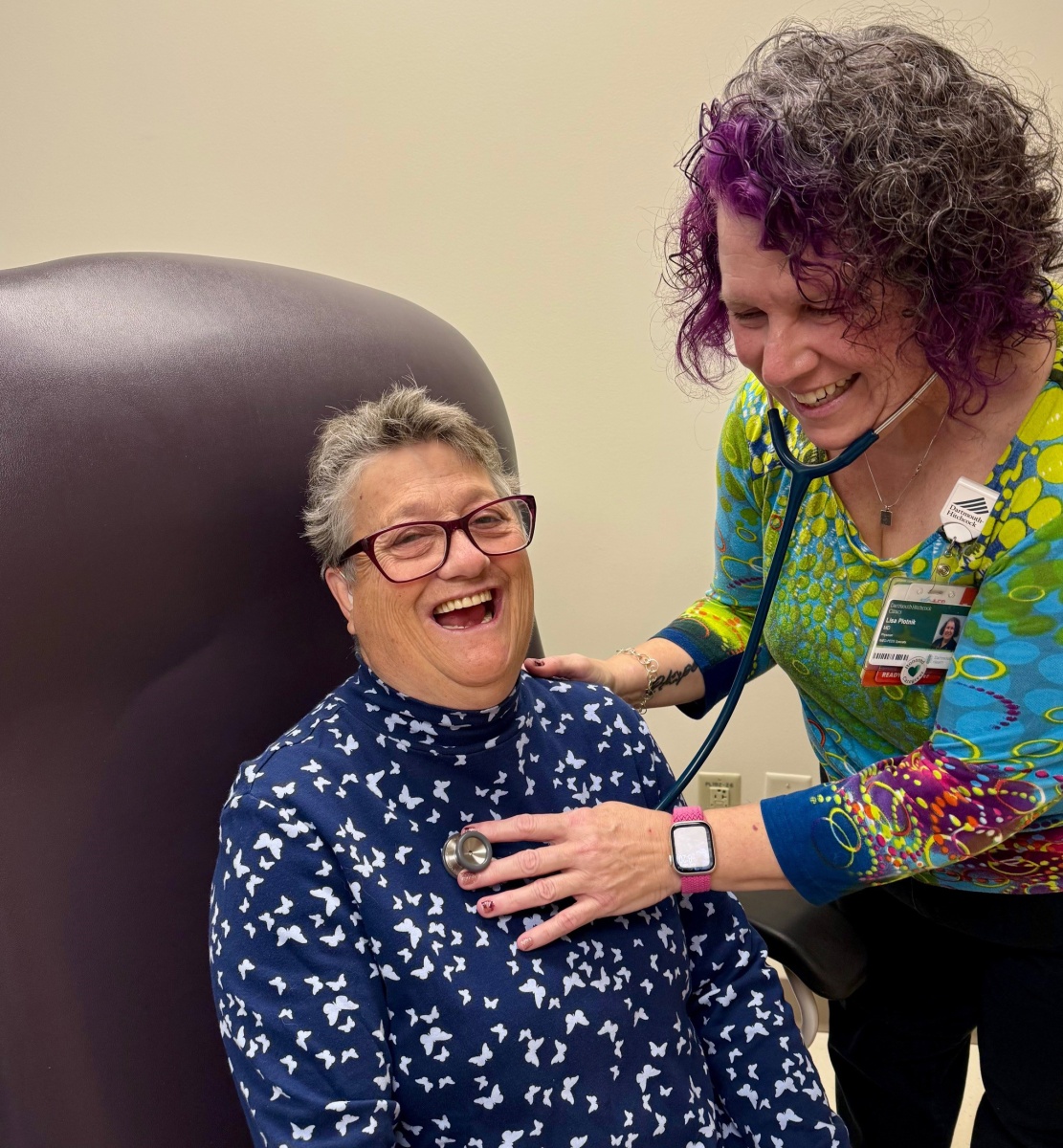 A female patient laughs as a female doctor uses a stethoscope