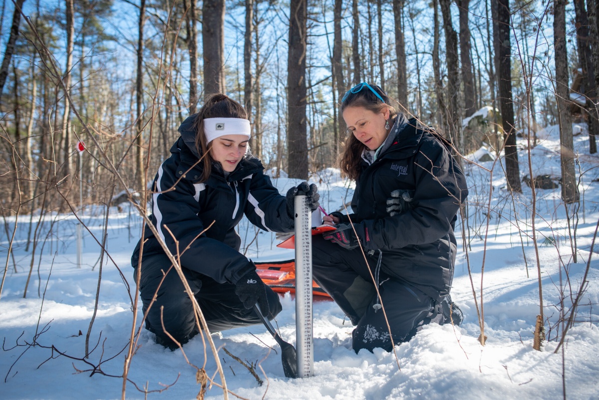Two female researchers kneel in the snow in front of a measuring instrument.