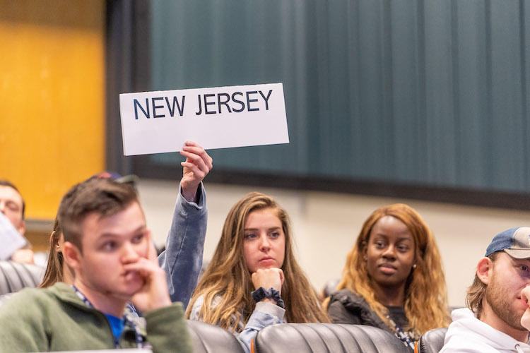 student holding up sign that reads 'New Jersey' during voting