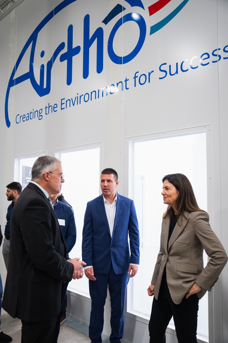 Three adults talk in front of a large sign that says AIRTHO