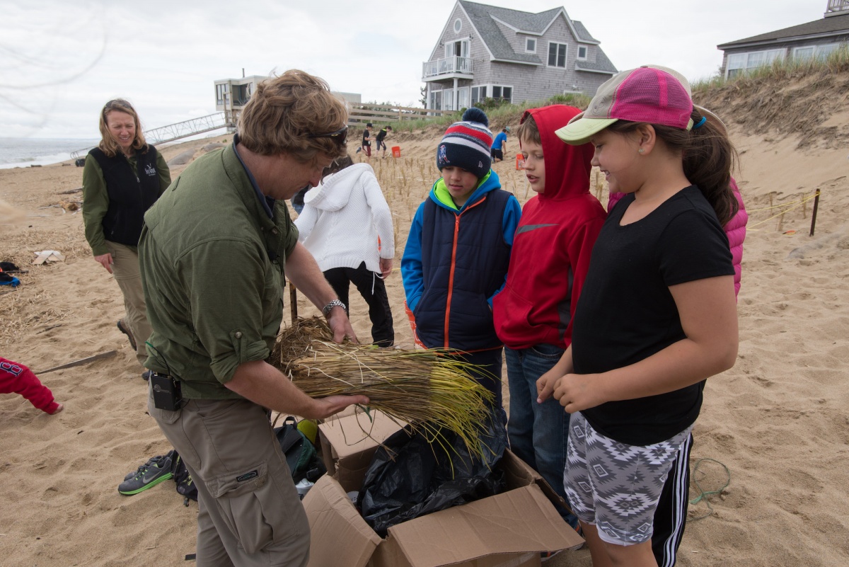 Researcher shows dune grass to elementary school students on a beach