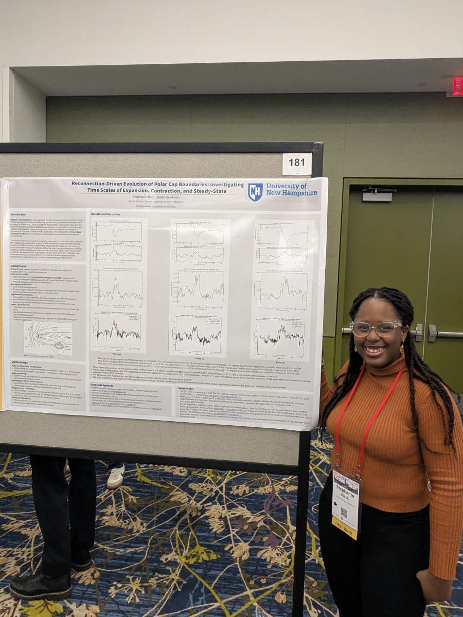 Young woman wearing glasses stands beside a scientific poster
