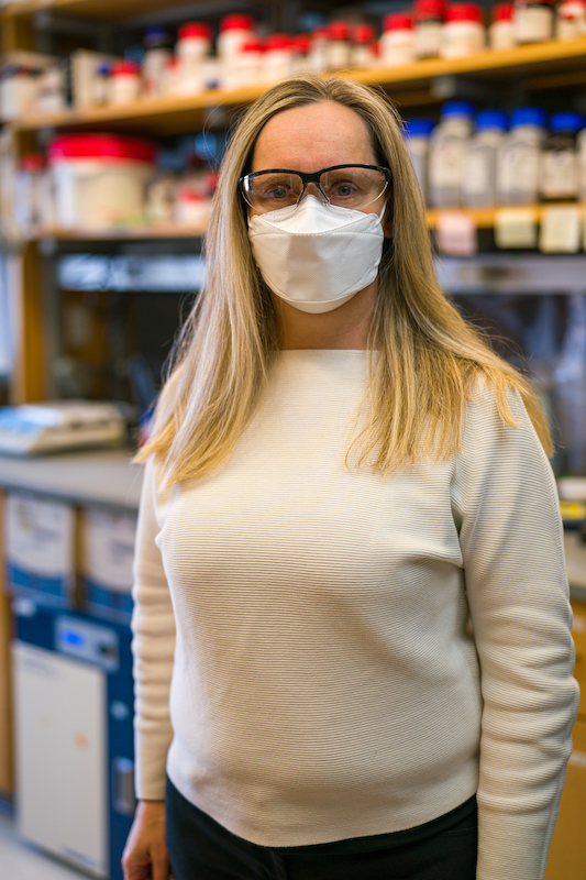 Female researcher wearing mask stands in lab looking at the camera