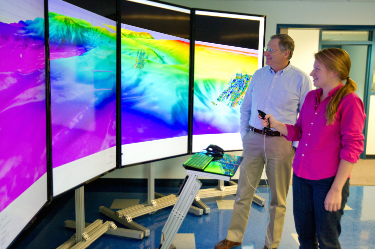 Two researchers in front of a brightly colored screen depicting the seafloor