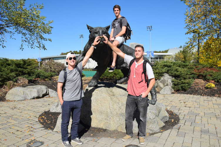 Three UNH students pose in front of the Wildcat statue. 