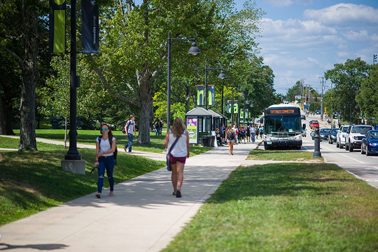 UNH students walking down Main Street by Thompson Hall Lawn in Durham