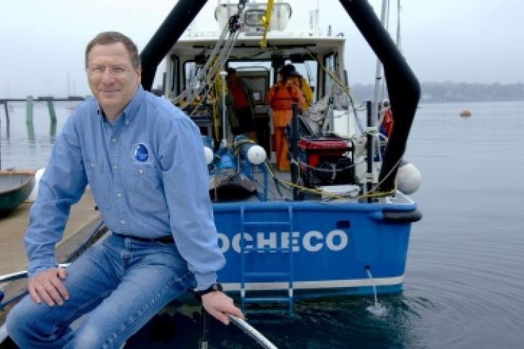 Larry Mayer sits on dock near research vessel.