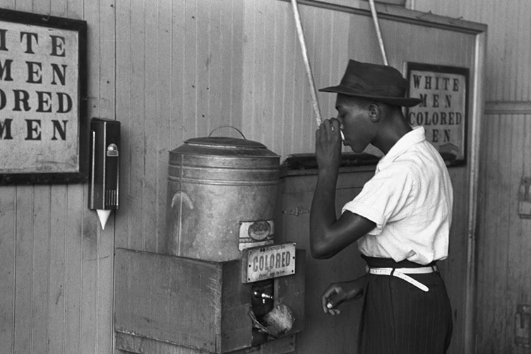 African American man drinking water from a keg labeled "colored"