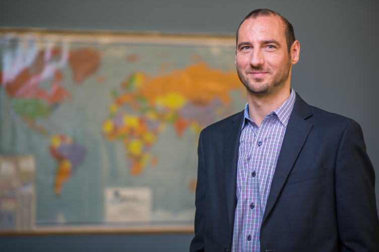 Associate Professor of Finance Milhail Miletkov standing in front of a world map