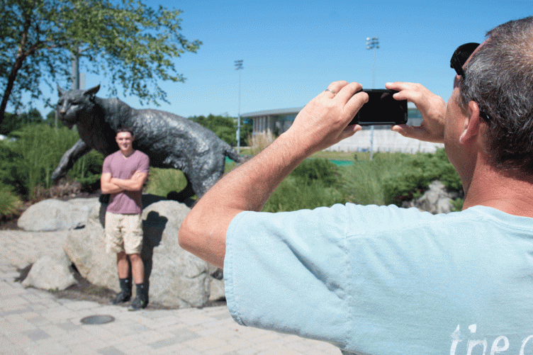 A parent takes a student's photo at the UNH Wildcat statue 