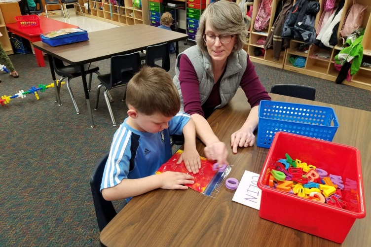 Photo of a teacher working with a student at a table in a classroom