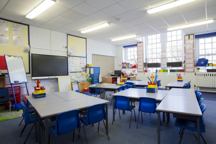 A photo showing an empty elementary school classroom, with desks and school supplies.