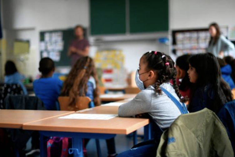 A young child sits at her desk in school with a face mask on. A young child sits at her desk in school with a face mask on.