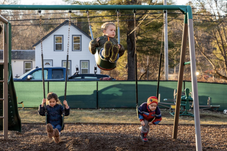 Children swing on swings outside of their early learning center in New Hampshire