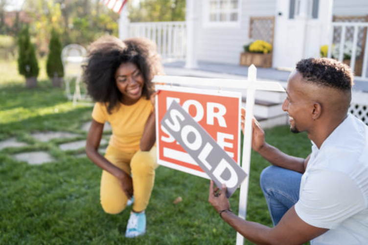 A couple places a "sold" sign on top of a "for sale" sign in their lawn.