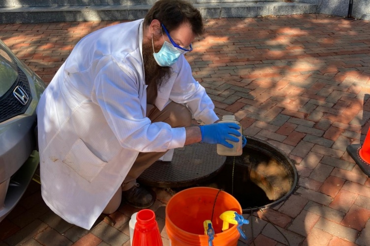 KELLEN SAWYER, A RESEARCH TECHNICIAN LEADING THE UNH SEWAGE MONITORING, RETRIEVES A SAMPLE FROM ONE OF THE MANHOLES 