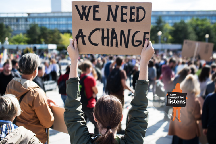 A photo showing a woman holding up a sign that says We Need A Change