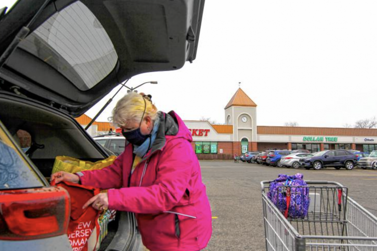 An elderly woman loads groceries into her trunk