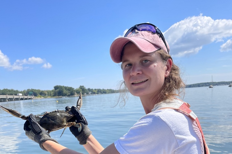 Female graduate student on a boat holding a male blue crab