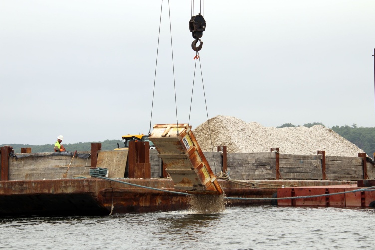 A crane drops seasoned shell into the water to establish substrate at the Nannie Island reef restoration site in Great Bay Estuary.