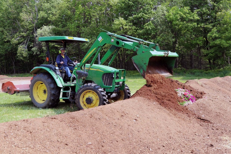 A photo of UNH Farm Manager Evan Ford in a tractor covering recently delivered compost at the Kingman Research Farm.