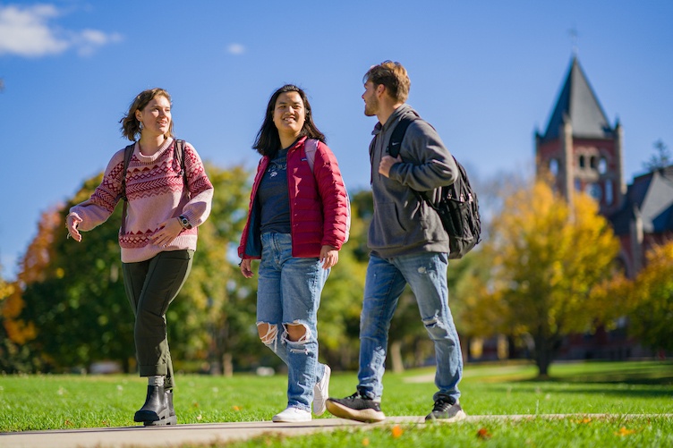 Three students walking on campus with Thompson Hall visible in the background