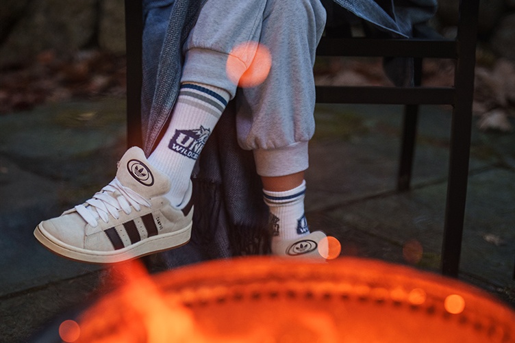 Close up shot of UNH socks on female student in front of a campfire