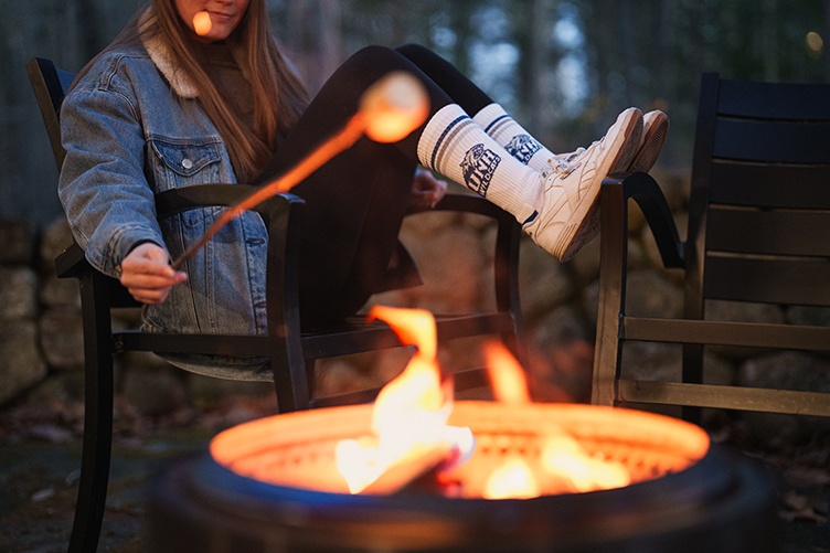 A woman wearing UNH socks roasts a marshmallow over a campfire