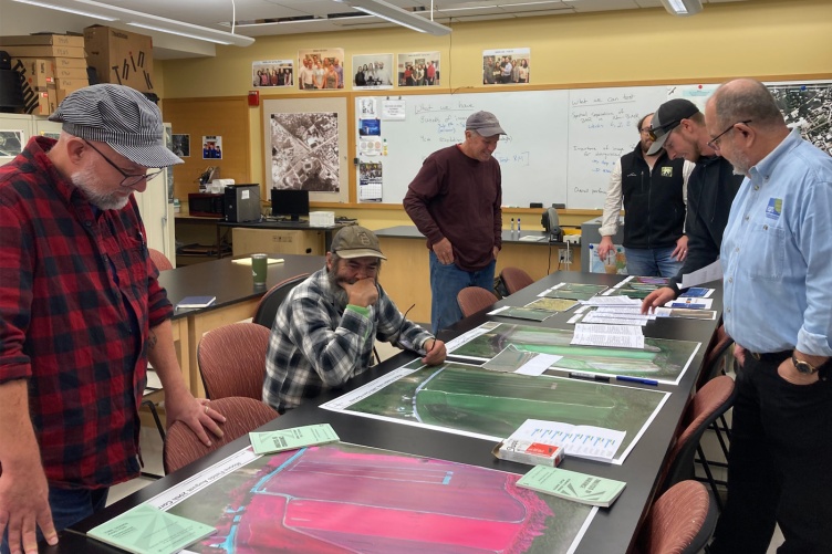 A group of men gathered around a table look at maps produced by a drone.