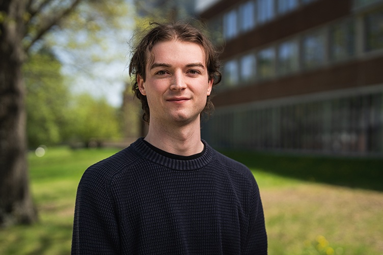 Portrait of male student standing in front of a tree outside of a brick building