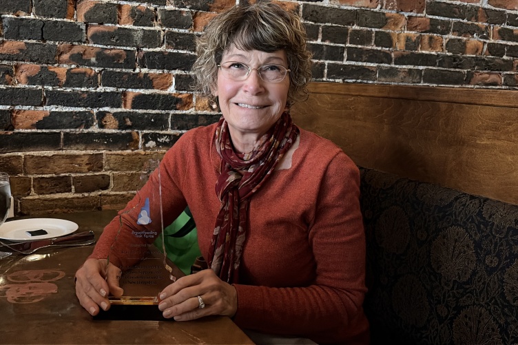 Karla Armenti sits in a restaurant booth holding an award and smiling