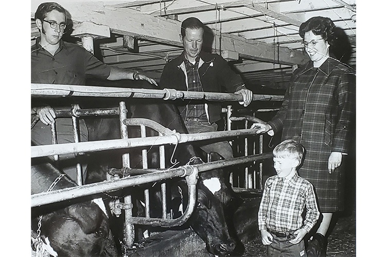 Two men and a woman stand with a child in a dairy barn in a black and white old photo