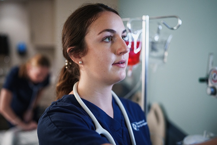 A nursing student wearing a stethoscope around her neck works in a hospital lab setting
