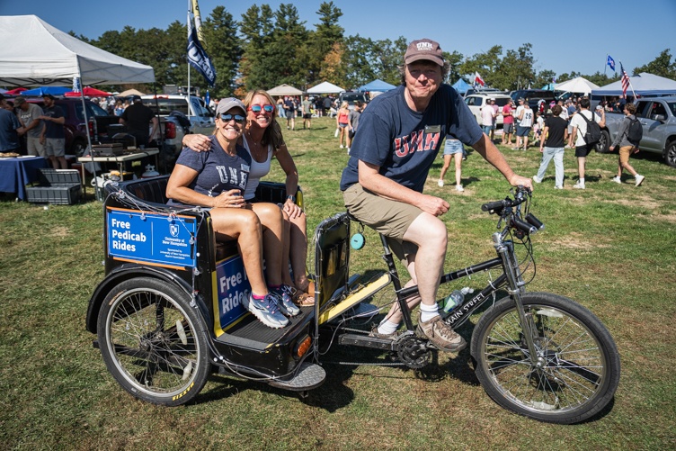 Two women ride in the back of a pedicab bicycle driven by a man in a baseball hat and t-shirt
