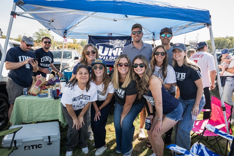 A large group of alumni pose for a photo under a tent