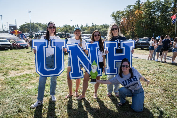 A group of three women hold up the letters U, N and H while a fourth woman kneels in front holding a small gnome doll in front of them