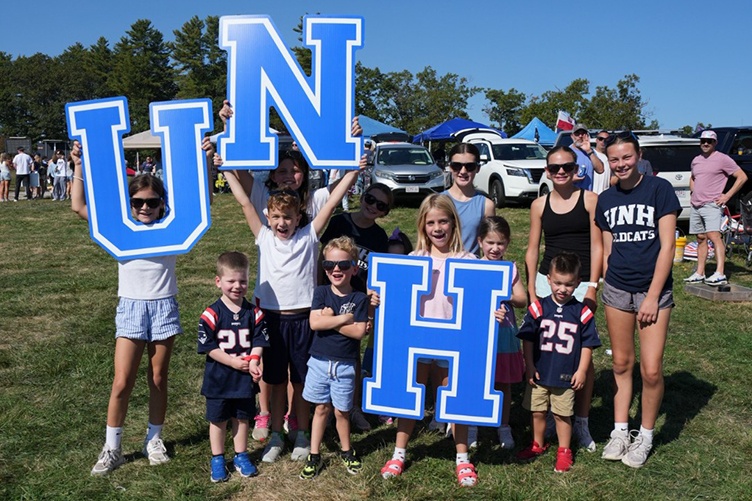 A group of young children gather, holding up the letters U, N and H