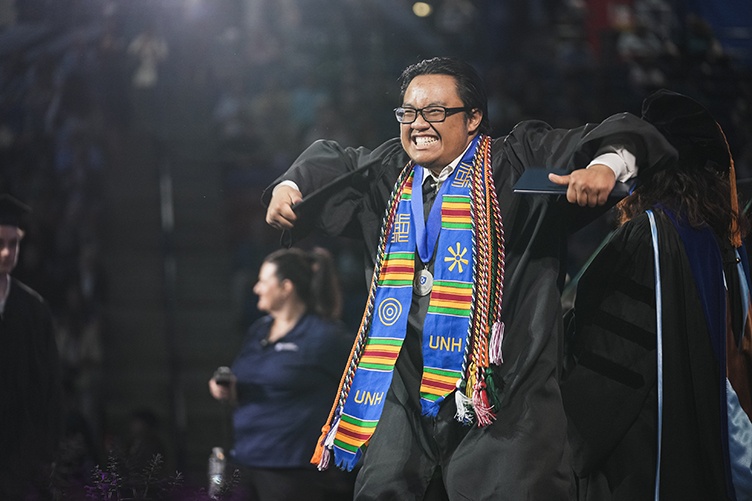 A male graduate in glasses pumps his arms in excitement after receiving his diploma