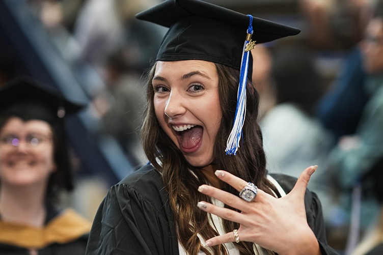 Female graduate in grad cap with huge smile shows a finger with a class ring on it