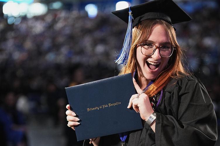 A female graduate smiles while displaying her diploma after walking across the stage
