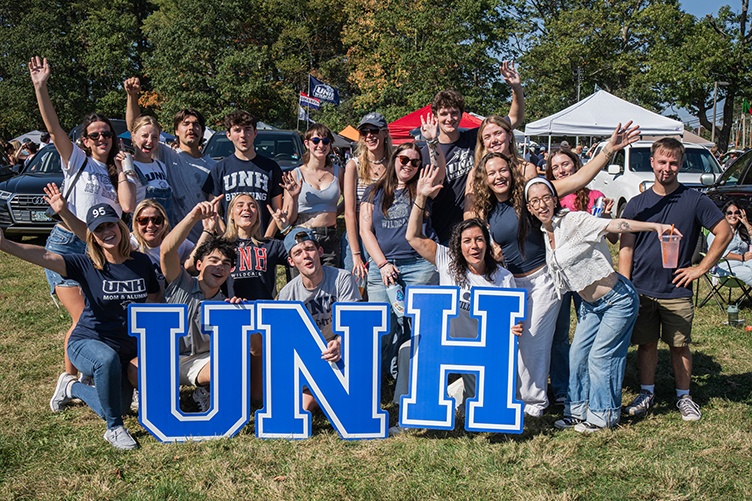 A large group of people gather behind the letters UNH at homecoming