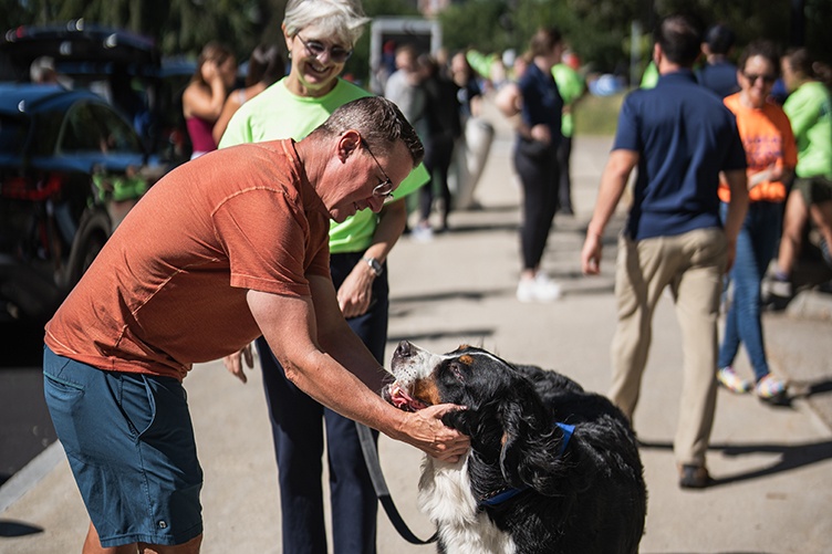 A man scratches a dog's chin as students move in to their dorm in the background