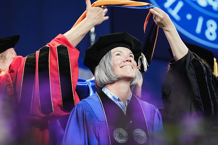 A woman graduate looks up as a commencement hood is placed over her shoulders