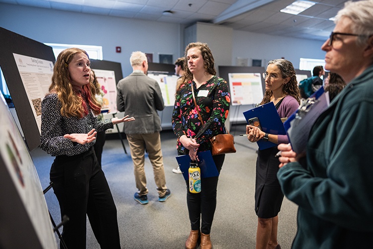 A group of three women stand in front of a female student who is standing in front of a poster