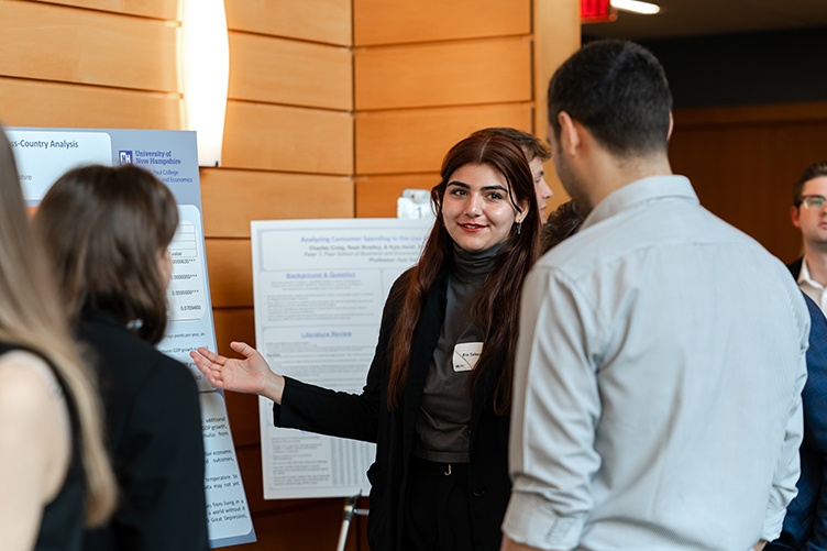 A woman points to a poster while speaking to a man and a woman