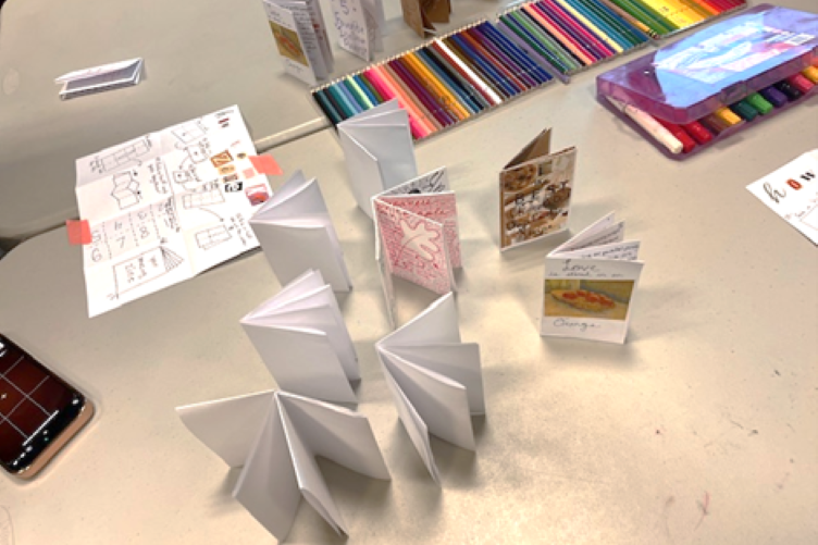 photo shows art supplies on table and done and in progress zines standing up