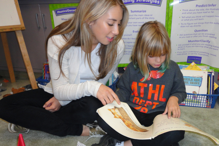 College student reading to younger student in literacy center