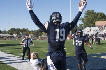 UNH football player holding football in the air