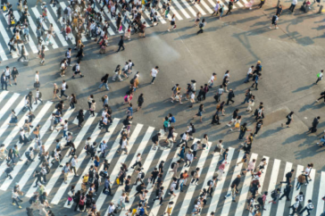 A large amount of people walk across cross walks
