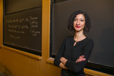 Physics professor Chanda Prescod-Weinstein stands against a chalkboard with arms crossed.